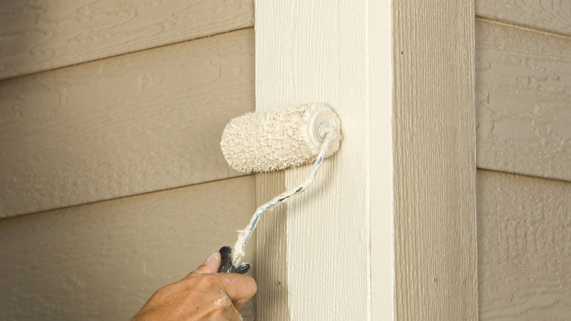 Paint roller applying white paint to wooden siding exterior wall