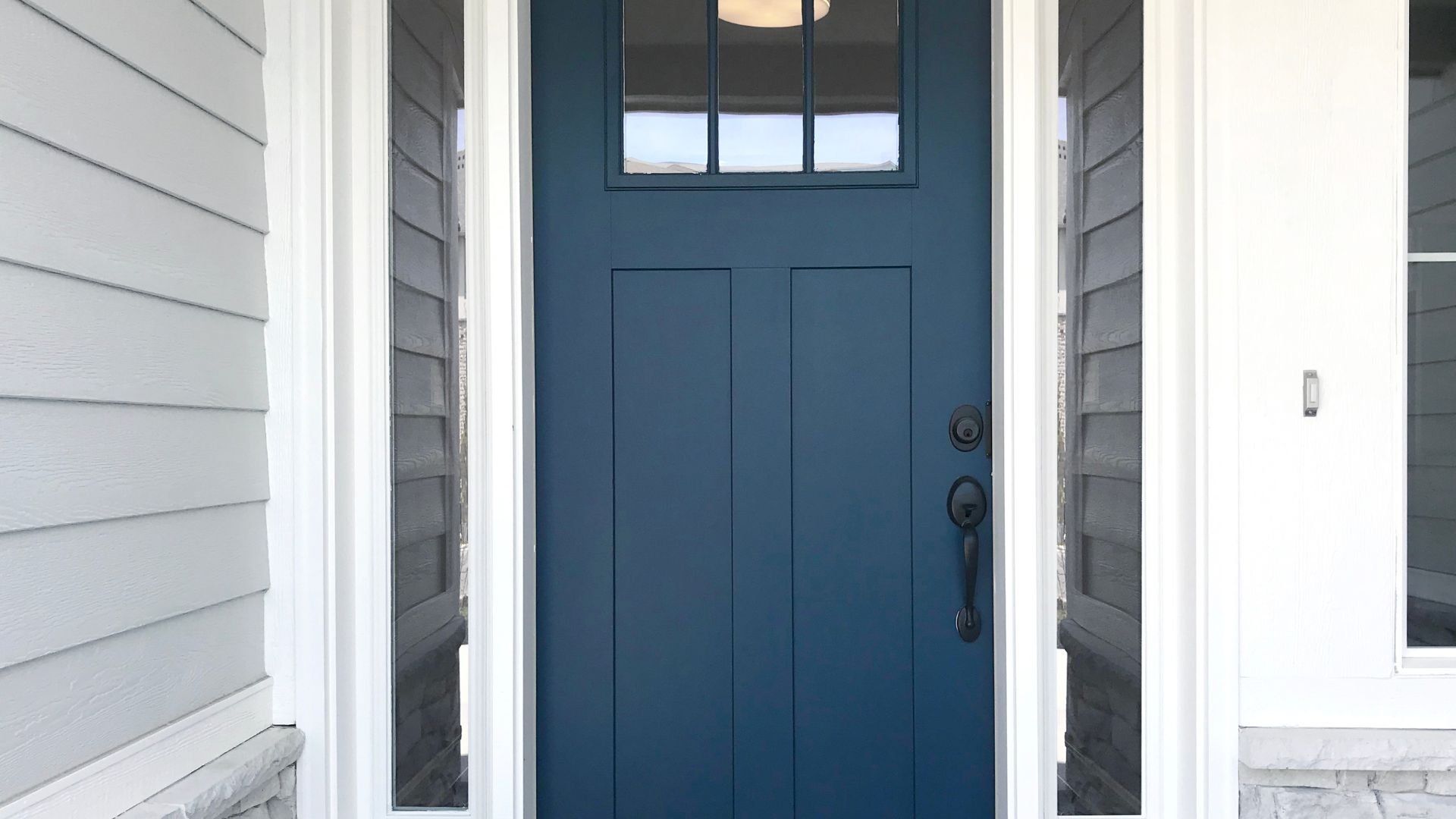 Blue front door with glass panels on a white and gray house exterior