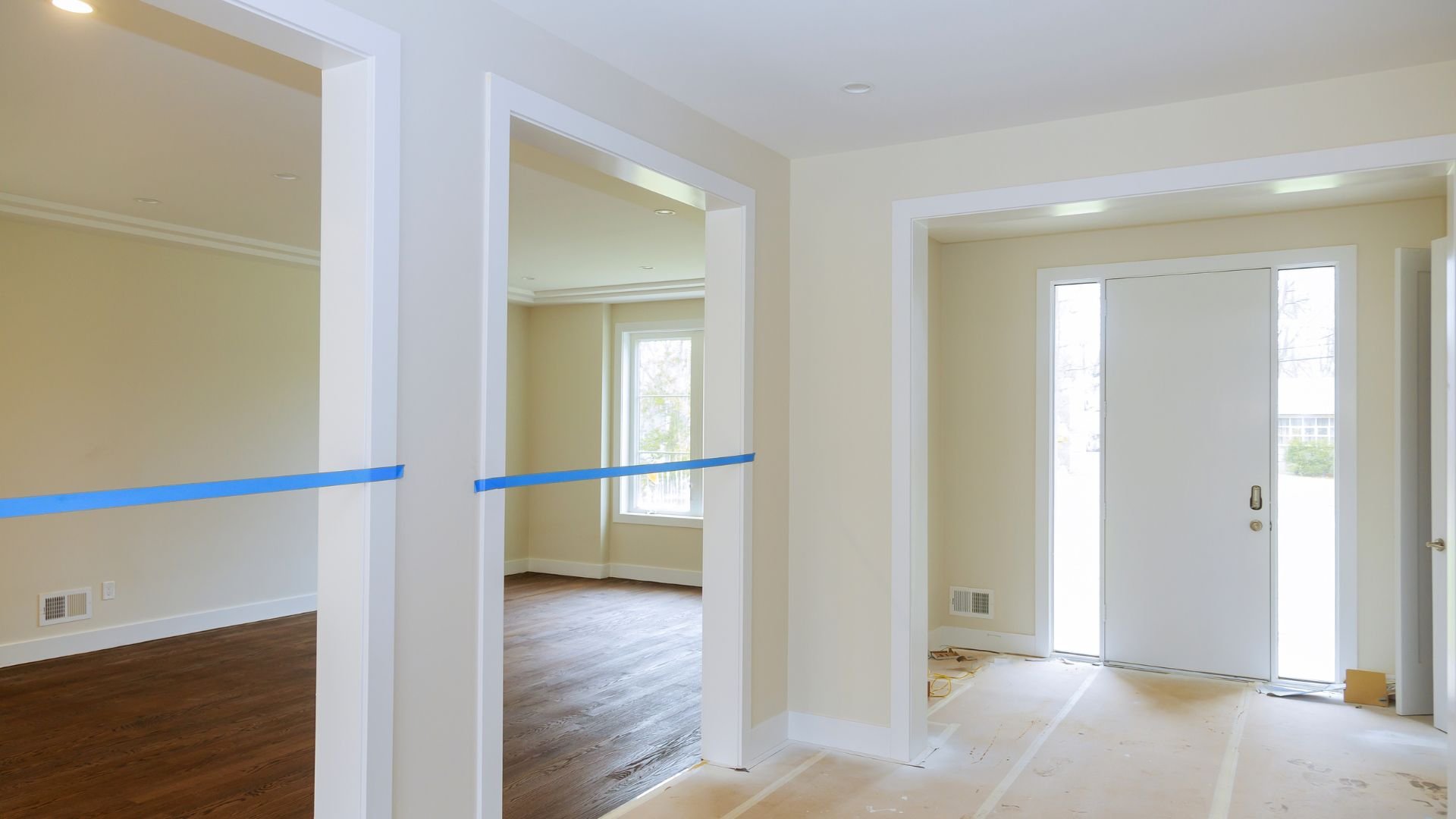 Empty rooms with white walls, blue tape, and hardwood floors during renovation