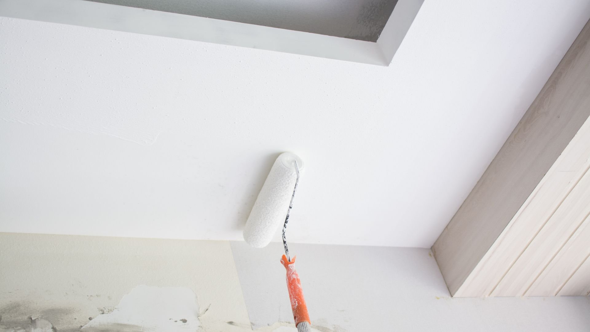 Paint roller with white paint rolling on ceiling during home renovation