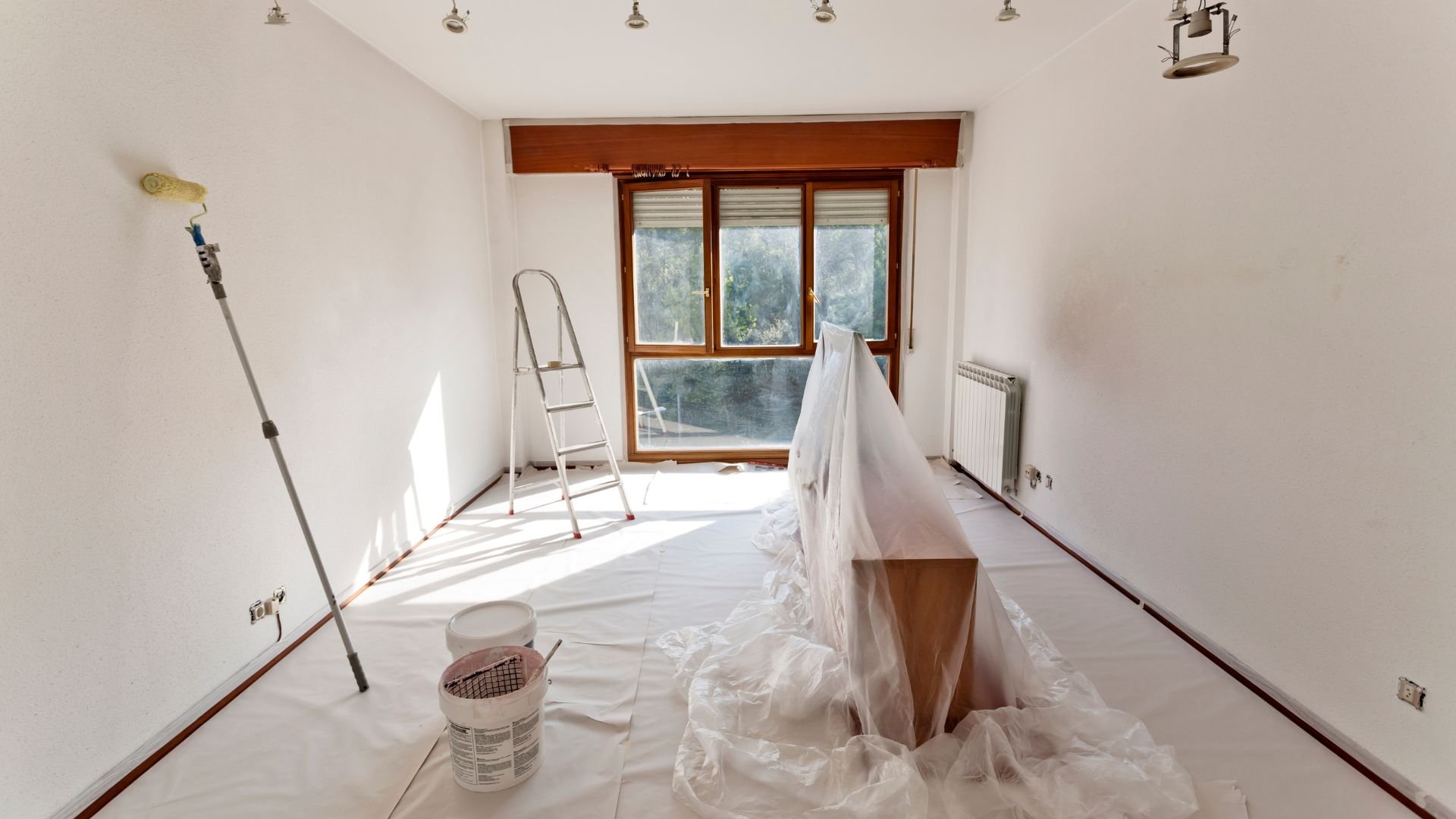 Room interior during renovation with paint supplies, ladder, and protective covers