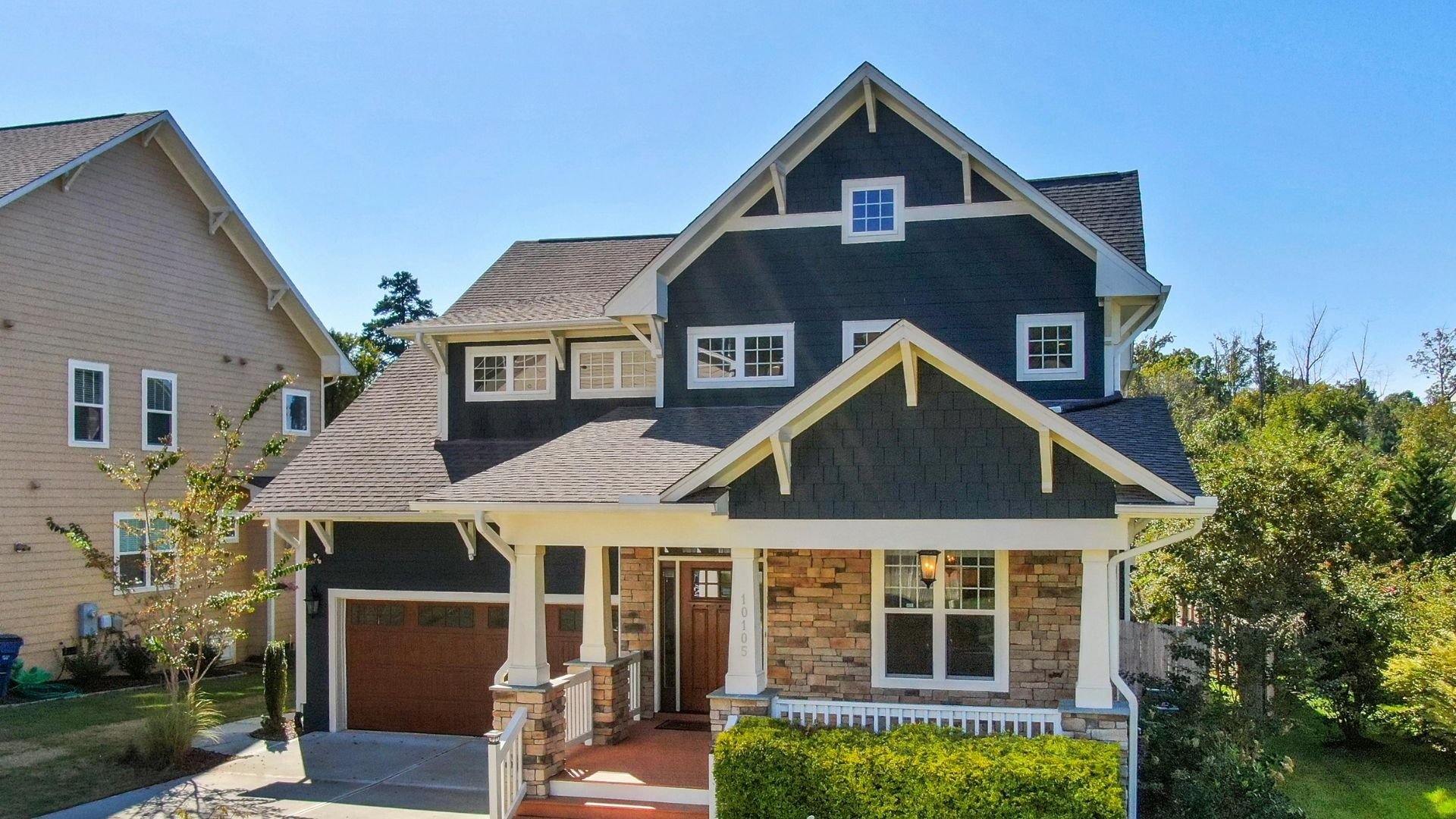 Craftsman-style two-story house with stone and dark blue exterior on sunny day