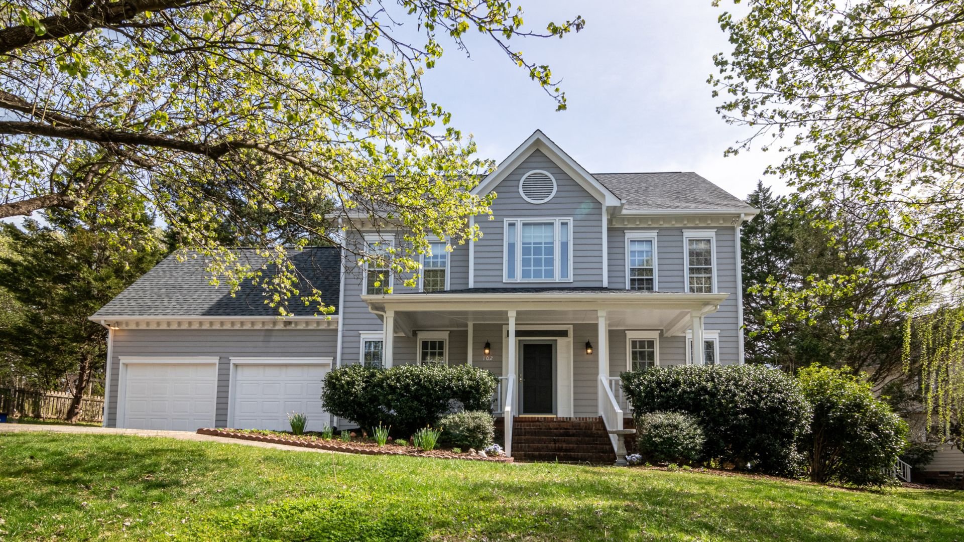 Two-story gray house with white trim, double garage, and spring trees