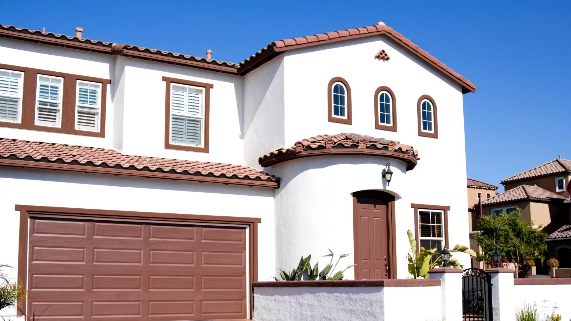 White Spanish-style two-story house with brown roof and garage