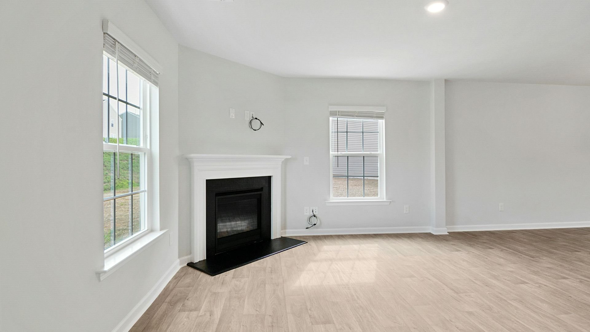 Empty room with white walls, fireplace, wood floor, and large windows
